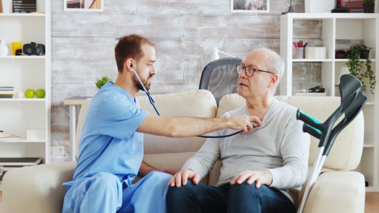revealing-shot-young-male-nurse-listening-old-retired-man-heartbeat-bright-cozy-nursing-home-caregiver-social-worker